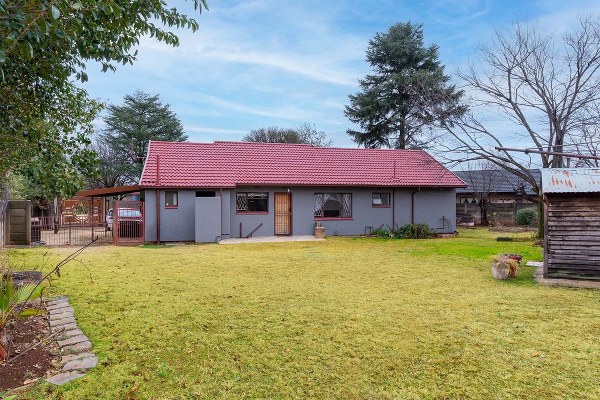 Rear view of the property featuring a tiled roof, security gates, and a spacious garden area with a concrete patio.