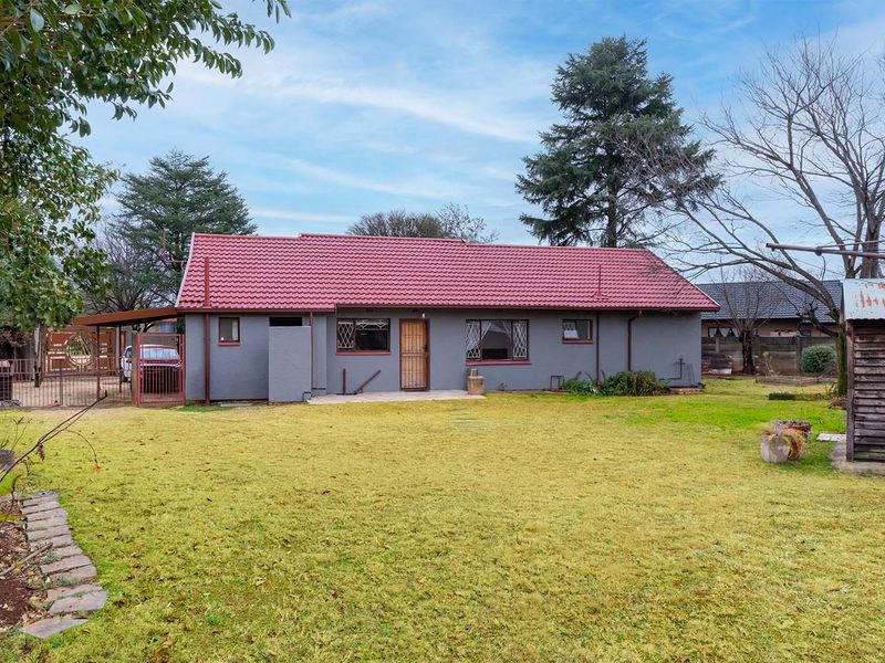 Rear view of the property featuring a tiled roof, security gates, and a spacious garden area with a concrete patio.
