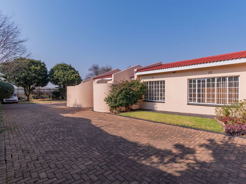 Front exterior view of the apartment featuring a paved driveway, well-maintained garden, and secure window bars.