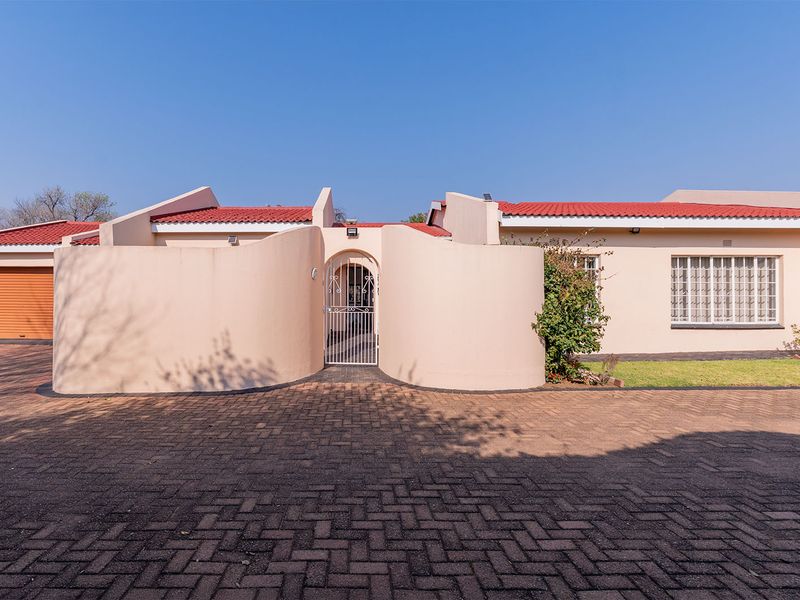 Front elevation of the apartment featuring a paved driveway, single garage, and a secure gated entrance with a tiled roof.