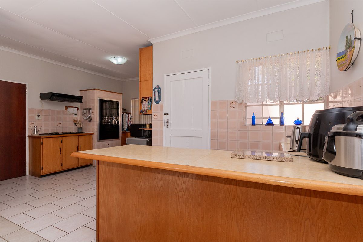 A functional kitchen featuring wooden cabinetry, laminate countertops, a built-in oven, and a hob, with a tiled backsplash and flooring throughout.