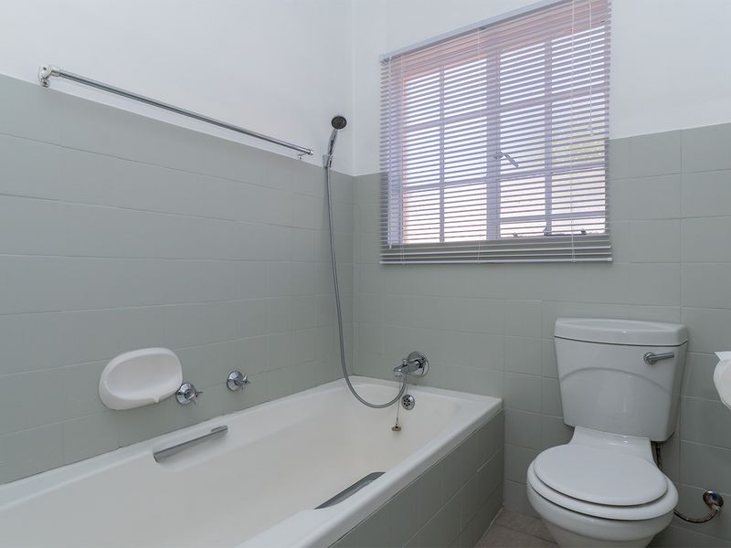 A functional bathroom featuring a bathtub with a handheld shower attachment, a standard toilet, and neutral wall tiling.
