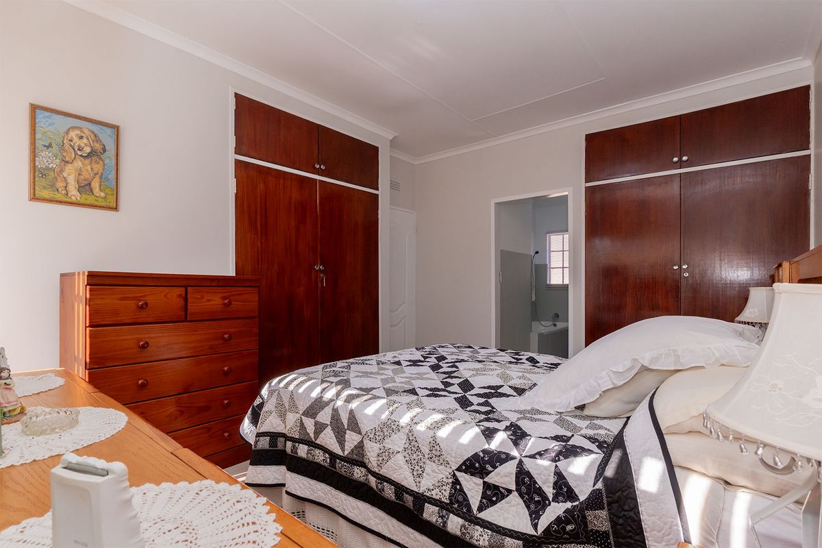 A bedroom featuring built-in wooden cupboards and direct access to an en-suite bathroom, offering a functional layout with classic finishes.