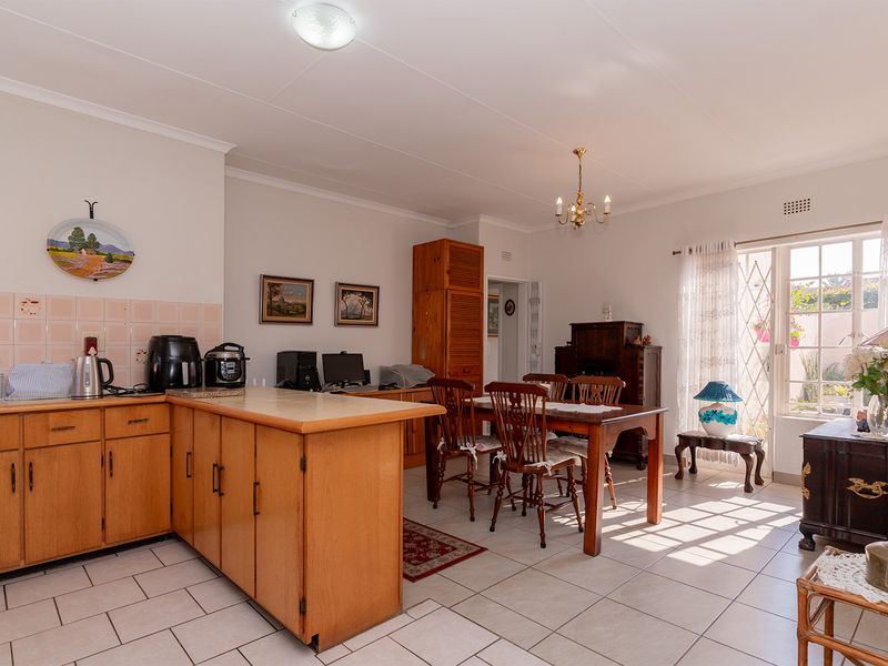 Open-plan kitchen and dining area featuring tiled flooring, built-in wooden cabinetry, and natural light through a glass-paneled door leading to the exterior.