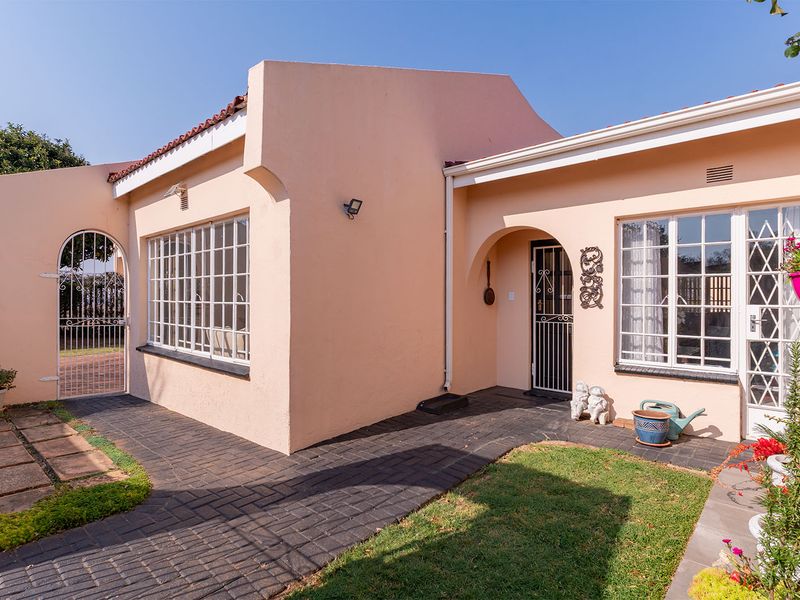 A well-maintained rear exterior view of the apartment featuring a paved walkway, security gates, and classic metal-framed windows.