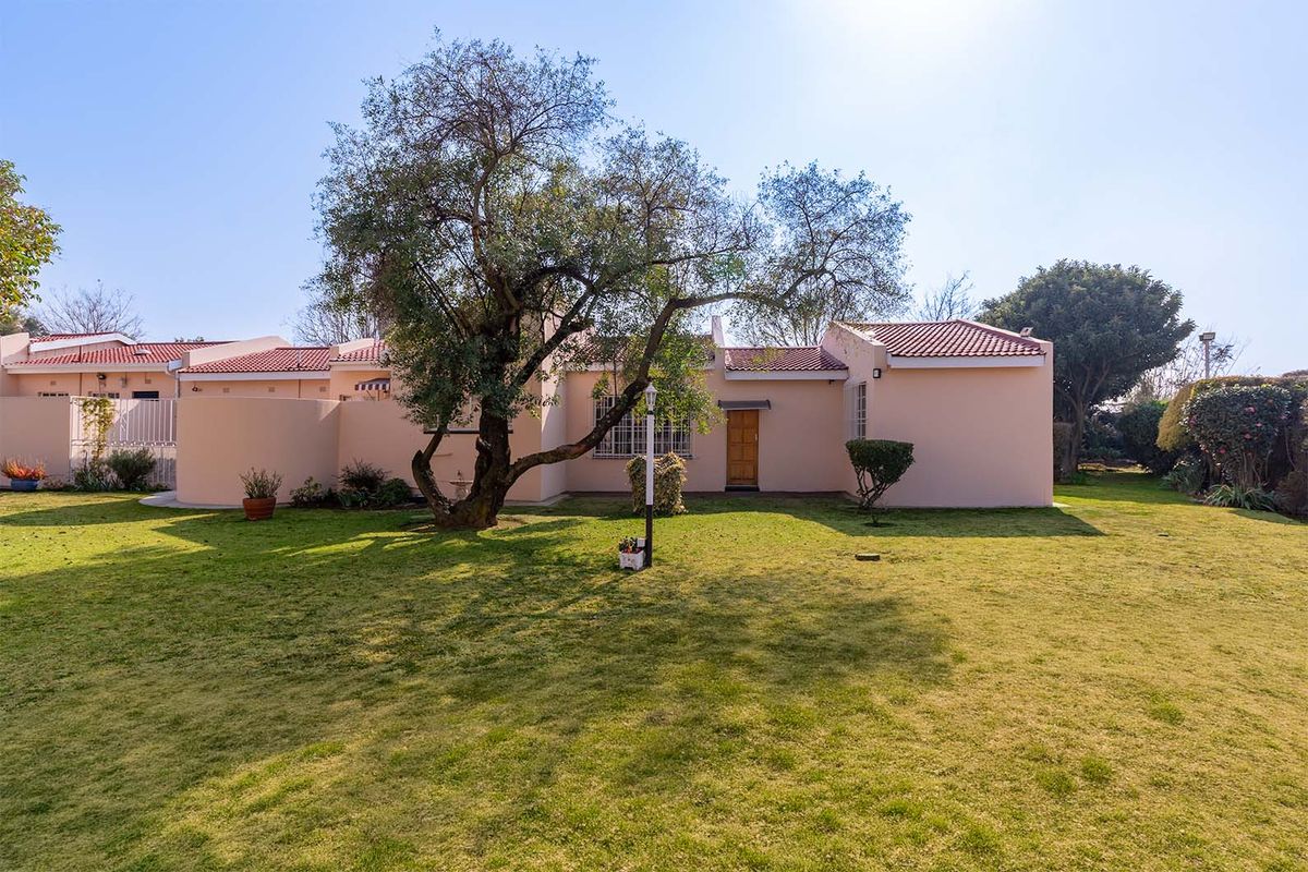 A view of the rear exterior of the apartment, featuring a private garden, mature tree, and tiled roof structure.