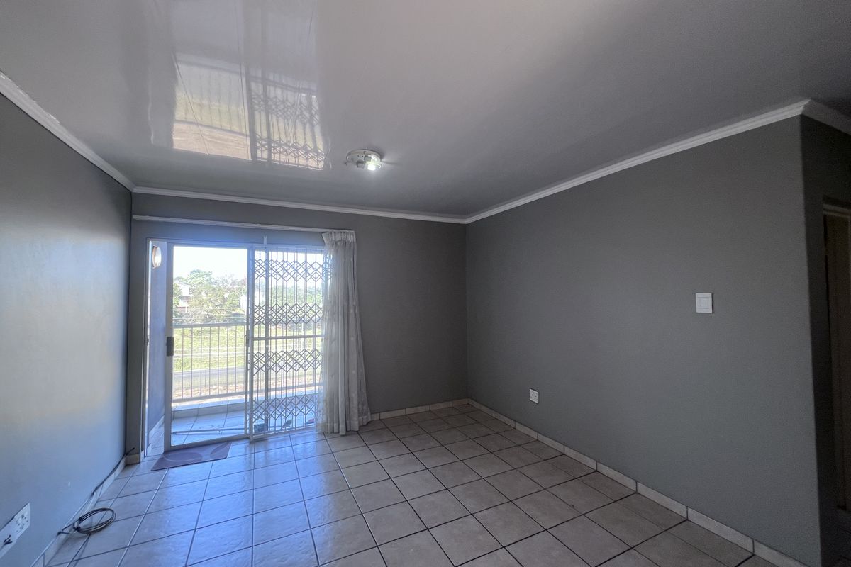 An empty living room featuring tiled flooring, a glossy ceiling, and a sliding glass door with a security gate leading to an outdoor area.