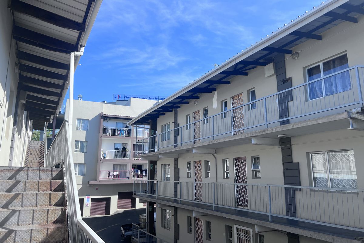 Exterior view of a multi-story apartment complex featuring metal staircases, open-air walkways, and security gates on unit entrances.