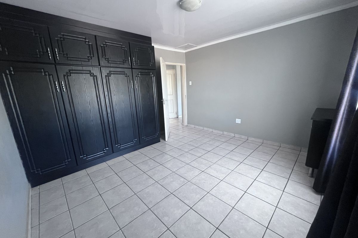 A spacious bedroom featuring neutral grey walls, large dark built-in cupboards, and clean tiled flooring, offering a versatile space ready for furnishing.