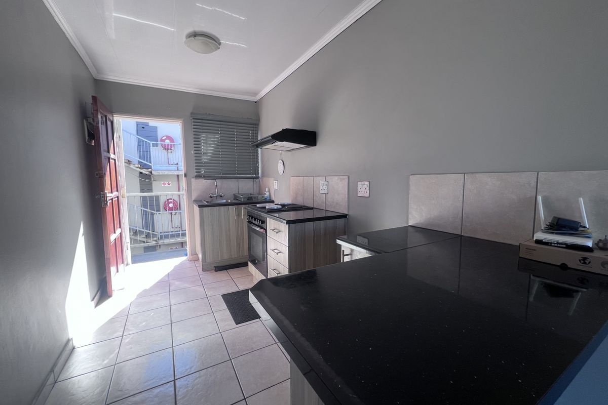 A functional kitchen featuring built-in cabinetry, black granite countertops, a built-in oven with extractor fan, and tiled flooring with direct access to an exterior area.