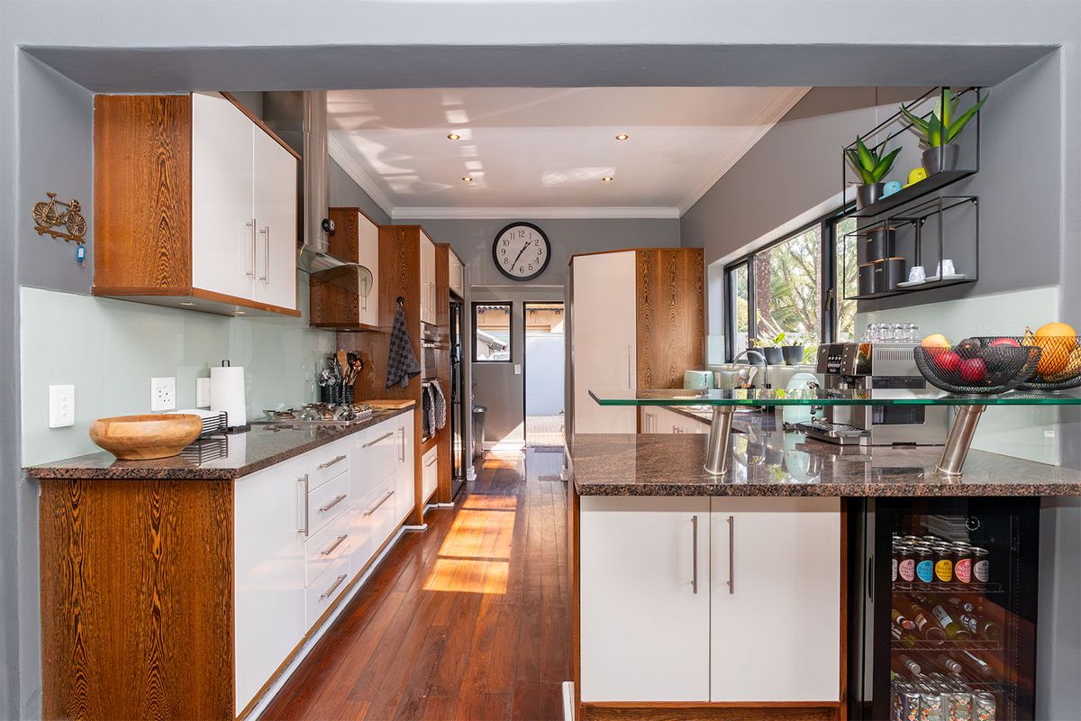 Modern kitchen featuring granite countertops, two-tone cabinetry, integrated appliances, a glass breakfast bar, and hardwood flooring with direct access to the rear exterior.