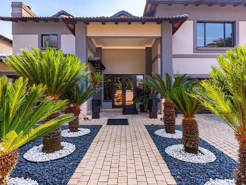 A well-maintained front facade featuring a paved walkway, covered entrance porch, and manicured garden beds leading to a modern double-door entry.