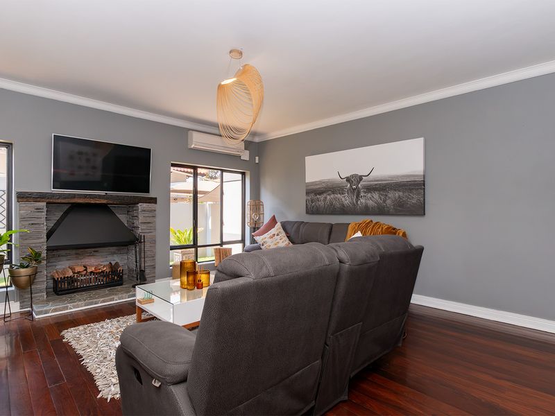 A well-maintained living room featuring dark timber flooring, a stone-clad fireplace with a timber mantel, and a wall-mounted split-system air conditioner.