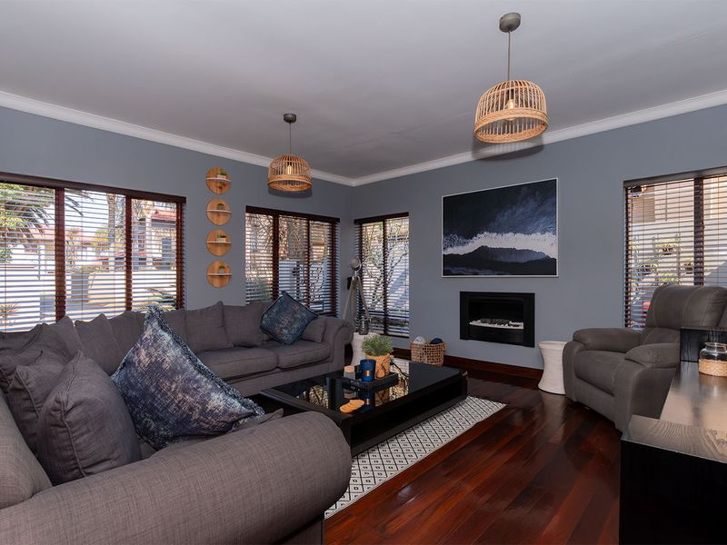 A well-maintained living room featuring rich hardwood flooring, a built-in fireplace, and large windows with venetian blinds, creating a comfortable and inviting atmosphere.
