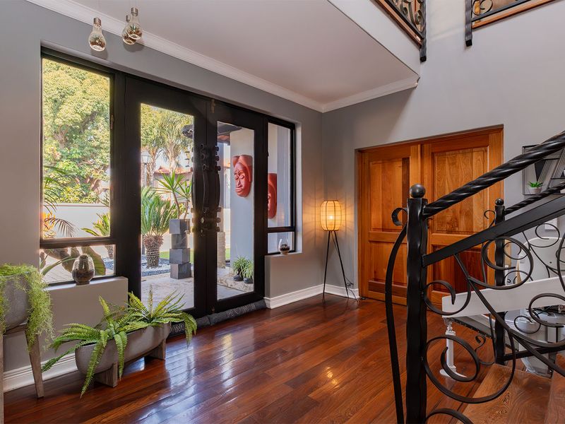 Spacious entrance hall featuring polished hardwood flooring, a decorative wrought iron staircase, and large glass doors providing natural light and garden views.