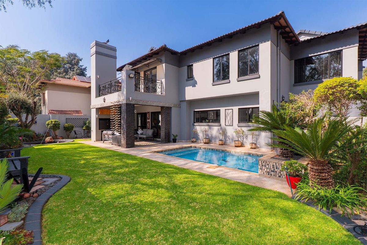 Rear view of a two-story house featuring a swimming pool, covered patio area, landscaped garden, and stone-clad architectural details.