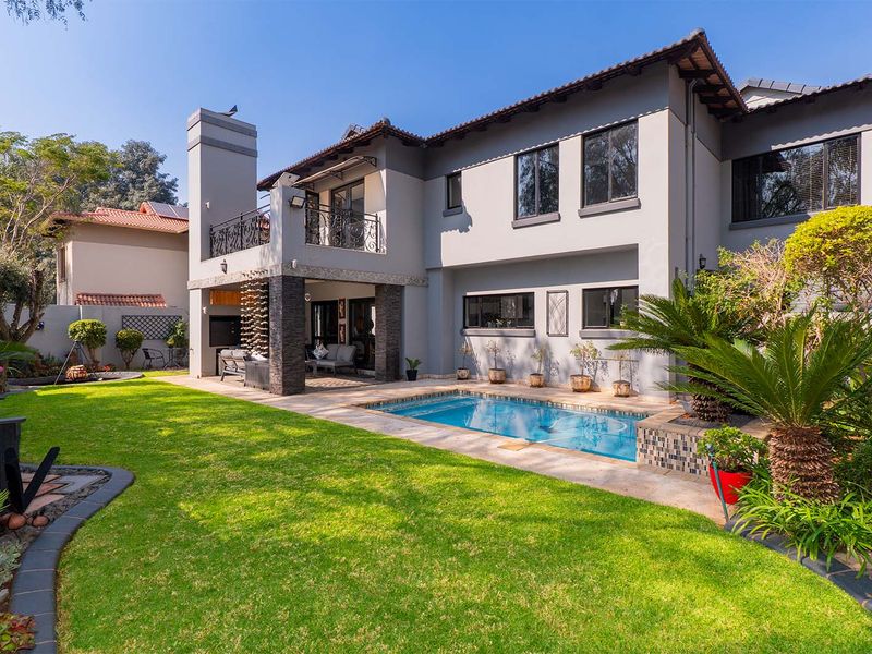 Rear view of a two-story house featuring a swimming pool, covered patio area, landscaped garden, and stone-clad architectural details.