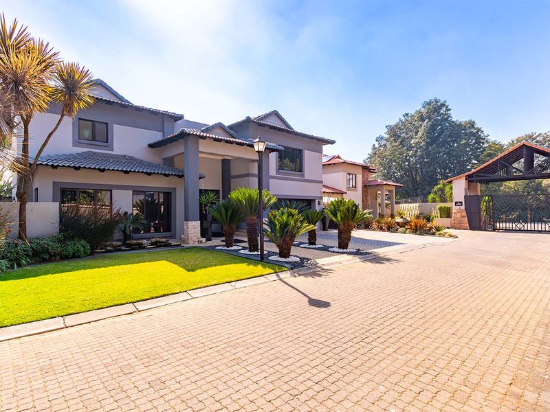 A well-maintained double-story residence featuring a paved driveway, landscaped garden, stone accents, and a secure gated entrance.