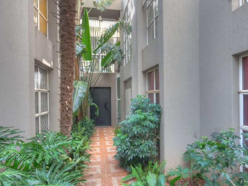 A private, landscaped courtyard area featuring a paved walkway between multi-story building sections with large windows and a secure entrance door.