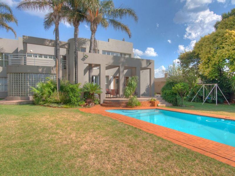 Rear view of the property featuring a swimming pool with brick coping, a covered patio area, and a spacious landscaped garden.