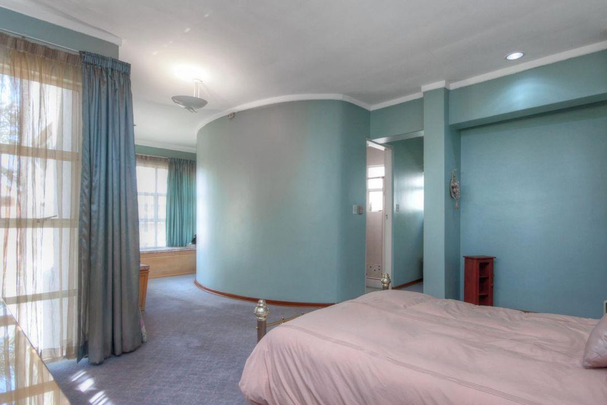 Spacious bedroom featuring a unique curved wall design, built-in window seating, and neutral carpet flooring with recessed lighting.