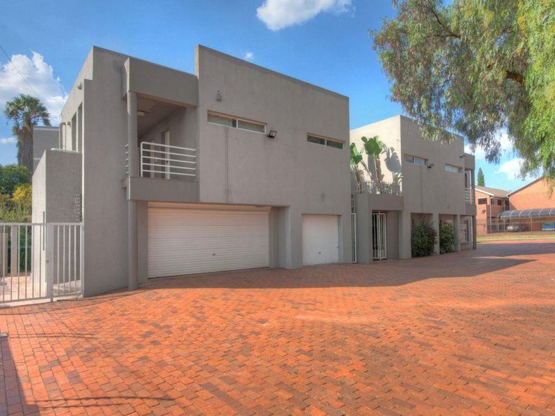 Front elevation of a modern multi-level townhouse complex featuring a paved driveway, multiple garage doors, and an upper-level balcony.