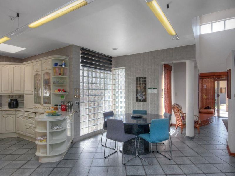 Open-plan kitchen and dining area featuring tiled flooring, classic cabinetry, and a distinctive glass block wall providing natural light.