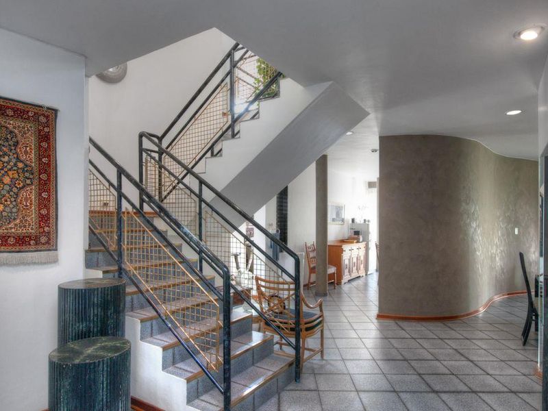 Spacious entrance hallway featuring a central staircase with metal balustrades, tiled flooring, and a distinctive curved feature wall.