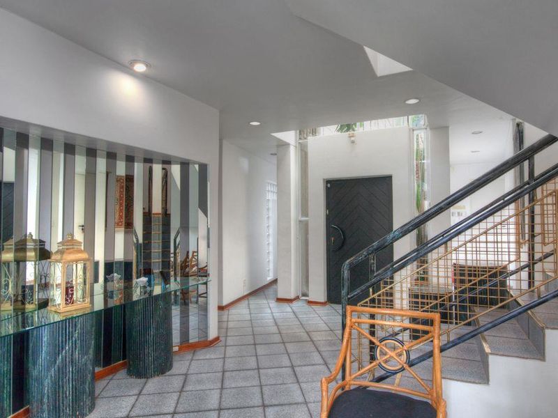 Spacious entrance foyer featuring tiled flooring, a prominent staircase with metal balustrades, a skylight, and decorative mirrored wall paneling.
