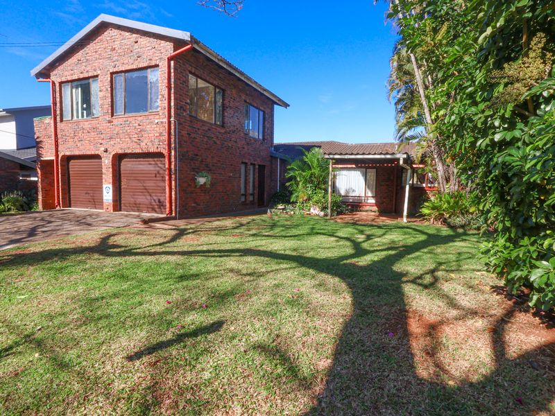 A two-story face brick residential property featuring a double garage, paved driveway, and a well-maintained front lawn with mature trees.