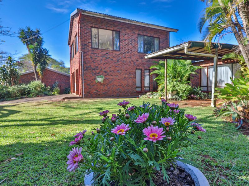 A view of the rear exterior of a double-story face brick house featuring a covered patio and a well-maintained garden.