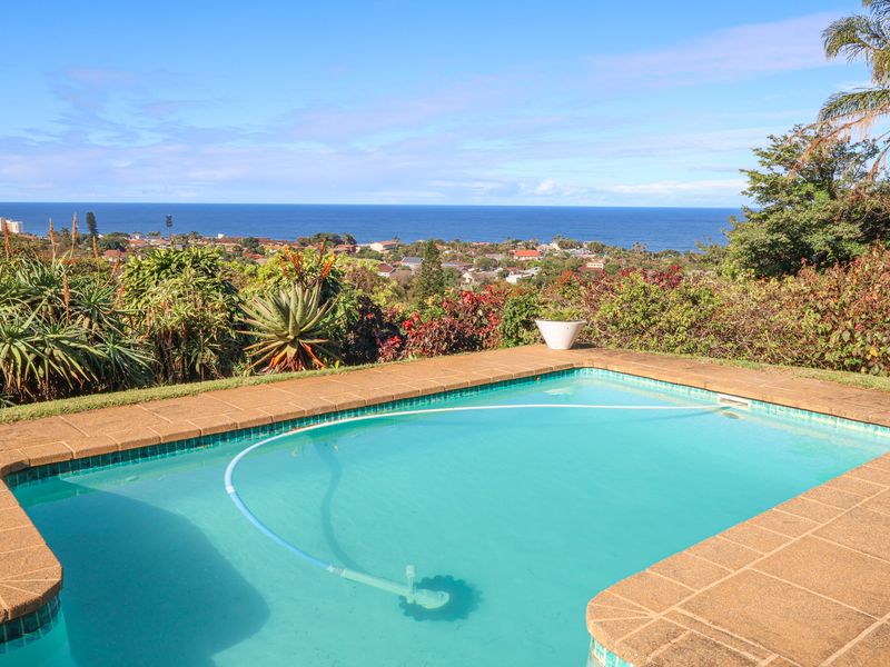 A well-maintained swimming pool with tiled coping, set within a landscaped garden offering expansive coastal and ocean views.