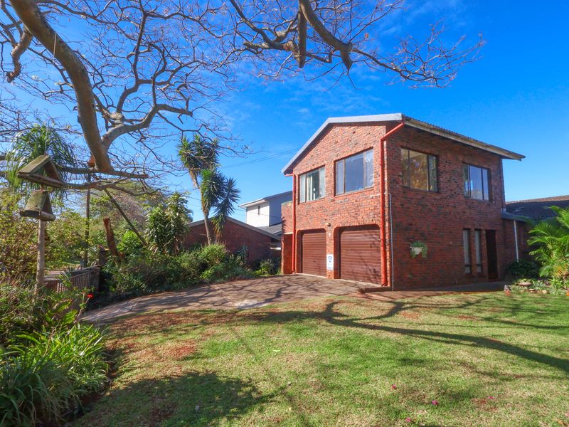 A well-maintained double-story face brick house featuring a double garage, paved driveway, and established garden setting.
