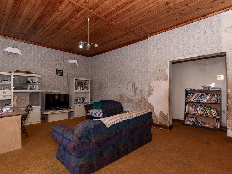 A living room featuring a timber tongue and groove ceiling, requiring significant wall and flooring restoration to improve its overall condition.