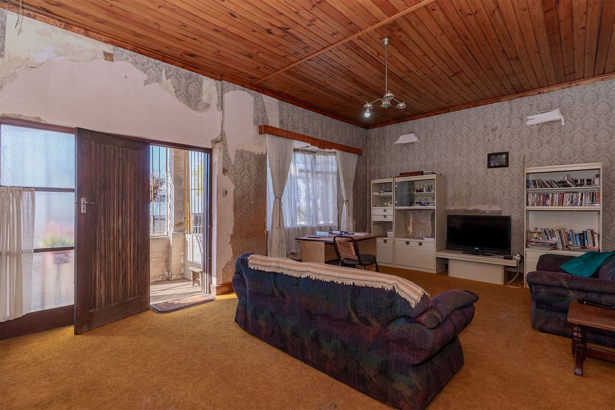 Spacious living room featuring a timber ceiling and direct access to an outdoor patio area, requiring significant cosmetic renovation and wall repairs.