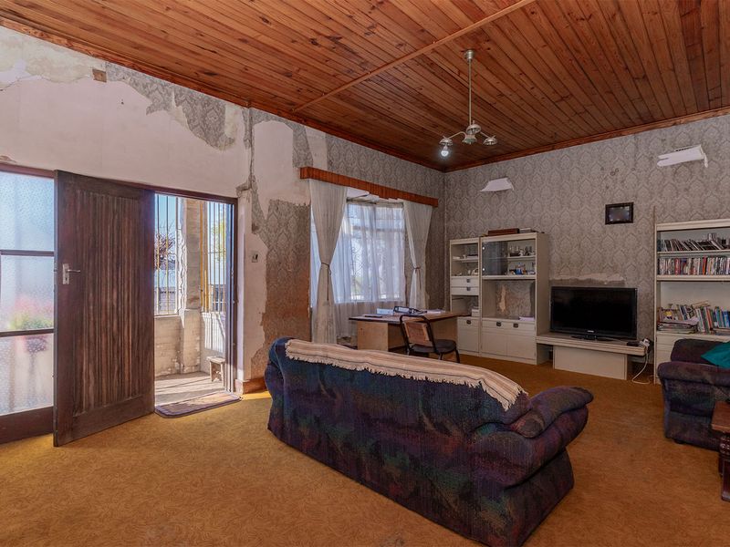 Spacious living room featuring a timber ceiling and direct access to an outdoor patio area, requiring significant cosmetic renovation and wall repairs.