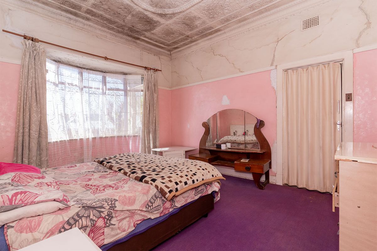 A bedroom featuring an ornate pressed metal ceiling, bay window, and folding door, currently requiring significant renovation due to wall and ceiling damage.