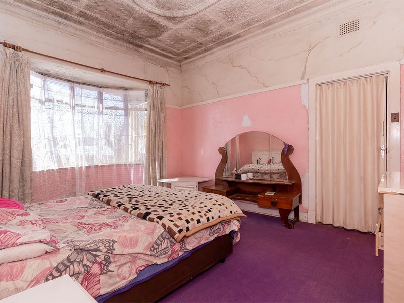 A bedroom featuring an ornate pressed metal ceiling, bay window, and folding door, currently requiring significant renovation due to wall and ceiling damage.