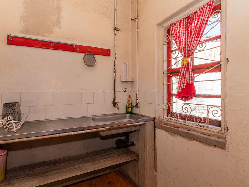 A functional laundry area featuring a stainless steel sink, tiled splashback, and a window with security bars, requiring cosmetic updates.