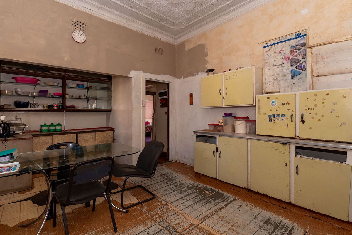 A dated kitchen featuring original cabinetry, pressed metal ceilings, and worn flooring, offering significant potential for a modern renovation and layout update.