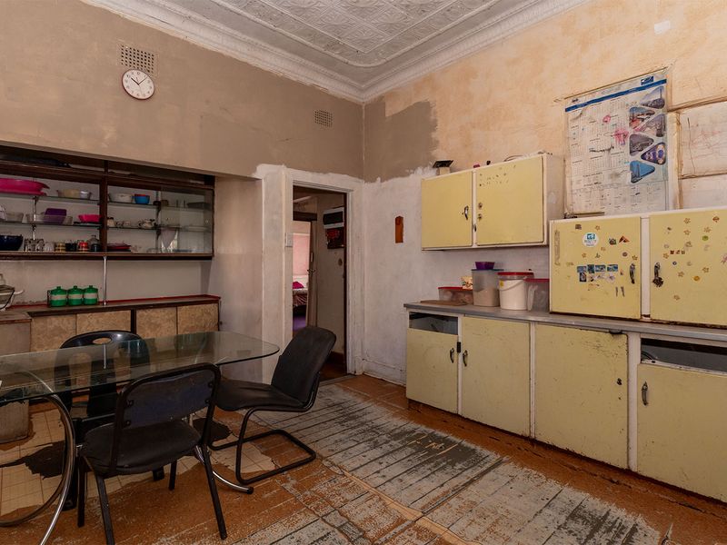 A dated kitchen featuring original cabinetry, pressed metal ceilings, and worn flooring, offering significant potential for a modern renovation and layout update.