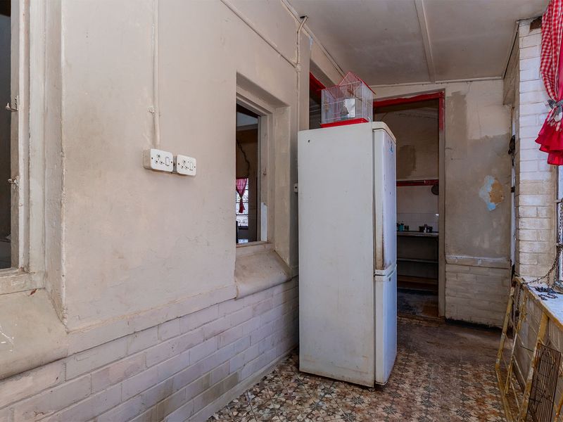 A dated scullery or utility area featuring exposed brickwork, tiled flooring, and an internal window connecting to the kitchen space.