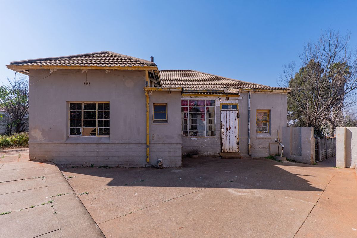 Rear view of a single-story house featuring a concrete patio, tiled roof, and original steel-framed windows requiring significant maintenance and restoration.