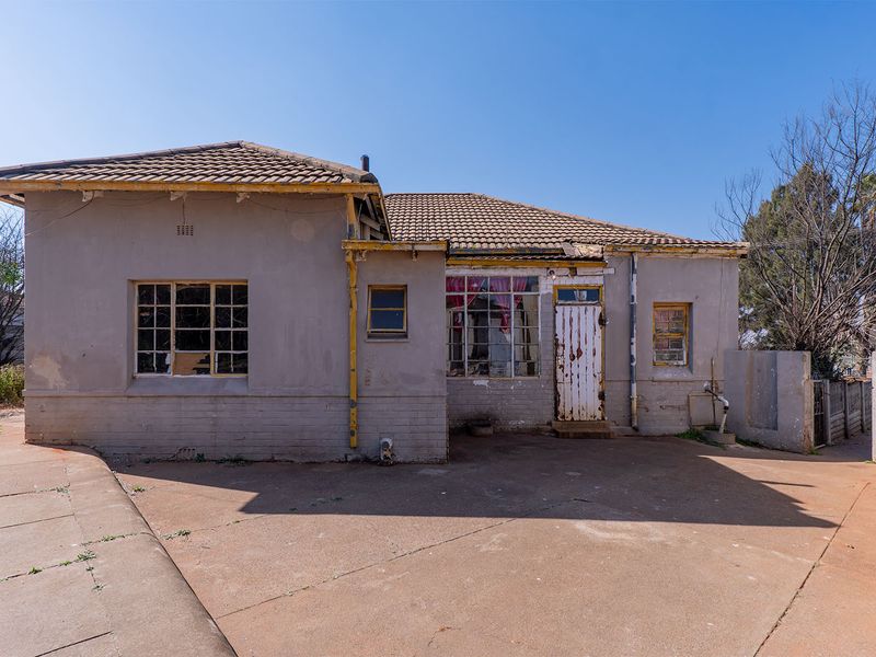 Rear view of a single-story house featuring a concrete patio, tiled roof, and original steel-framed windows requiring significant maintenance and restoration.
