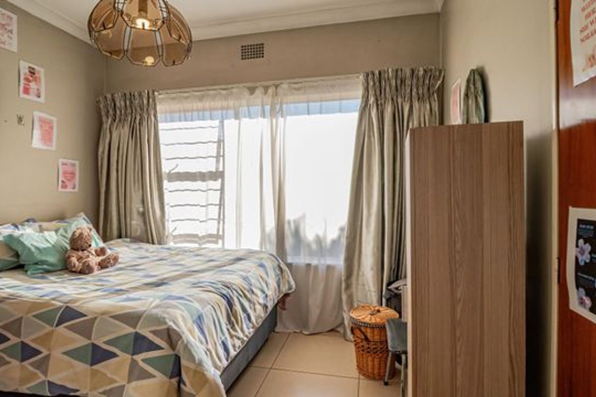 A bedroom featuring tiled flooring, a large window with curtains, and a ceiling light fixture.