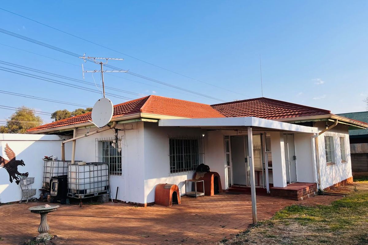 Rear view of the house featuring a covered patio area, brick paving, and security bars on the windows.