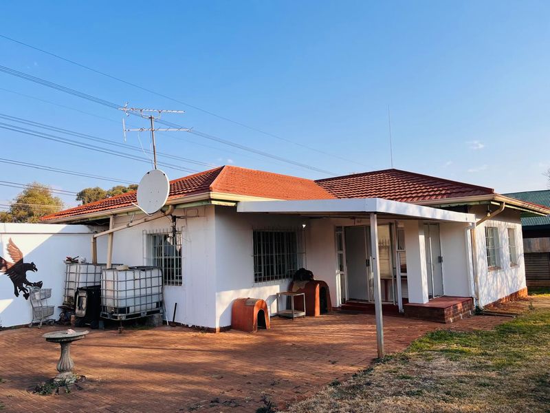 Rear view of the house featuring a covered patio area, brick paving, and security bars on the windows.