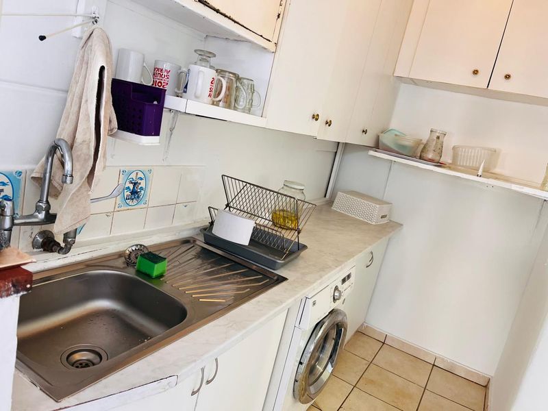 A functional laundry area featuring built-in cabinetry, a stainless steel sink, and tiled flooring, offering practical utility space with potential for cosmetic updates.