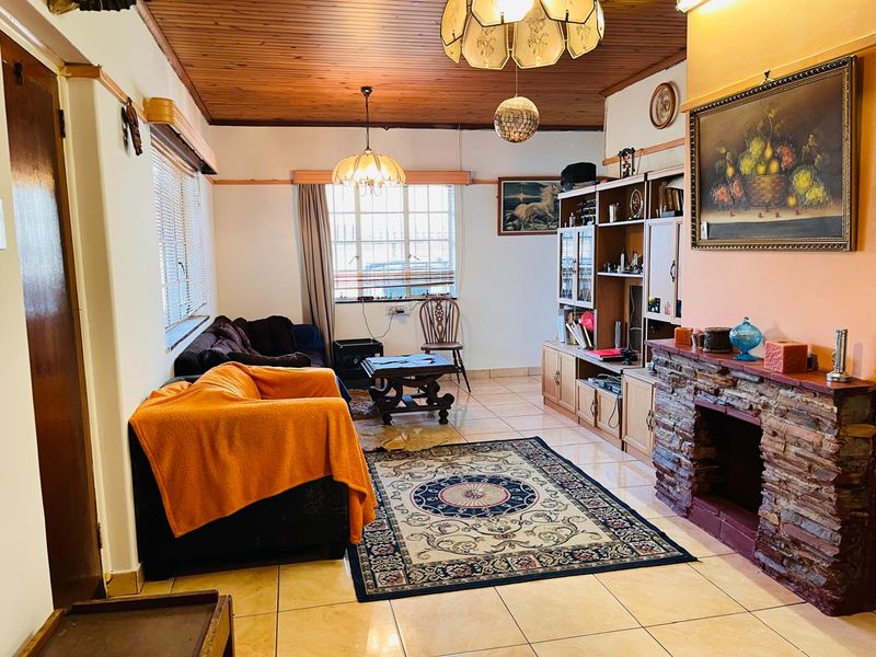A living room featuring a stone fireplace, timber-clad ceiling, and tiled flooring, offering a traditional layout with built-in storage cabinetry.
