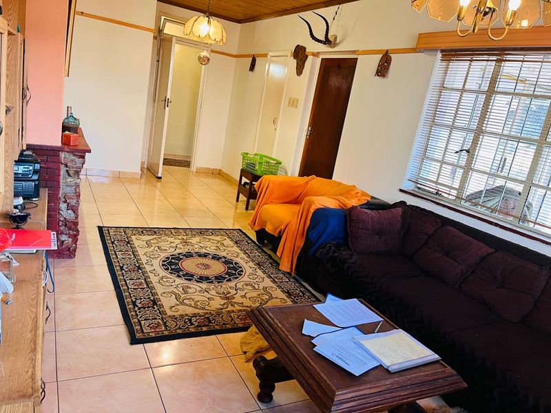 A living room featuring tiled flooring, a timber ceiling, and a brick fireplace, offering a dated aesthetic with potential for modernization.